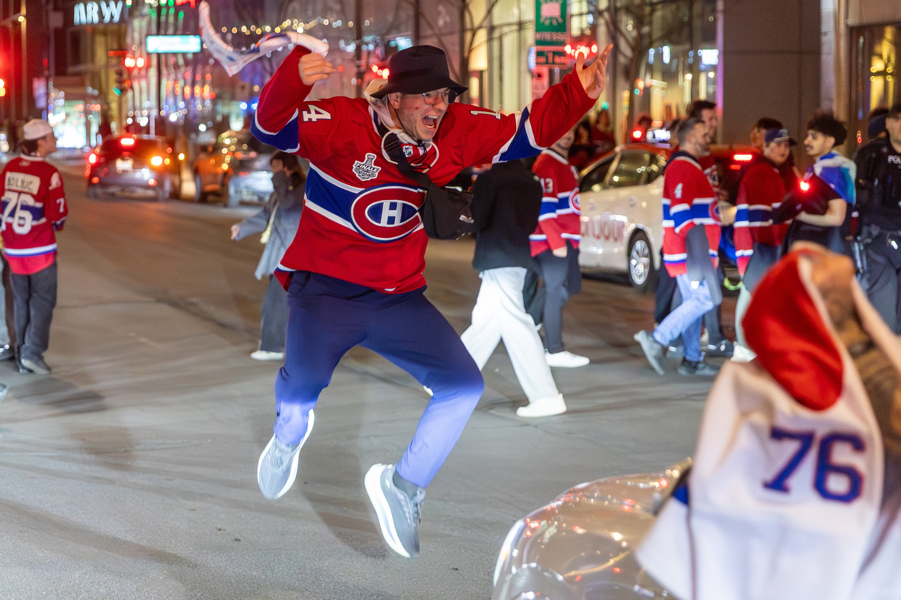 A Canadiens fan in a Habs jersey jumps for joy while crossing the street.