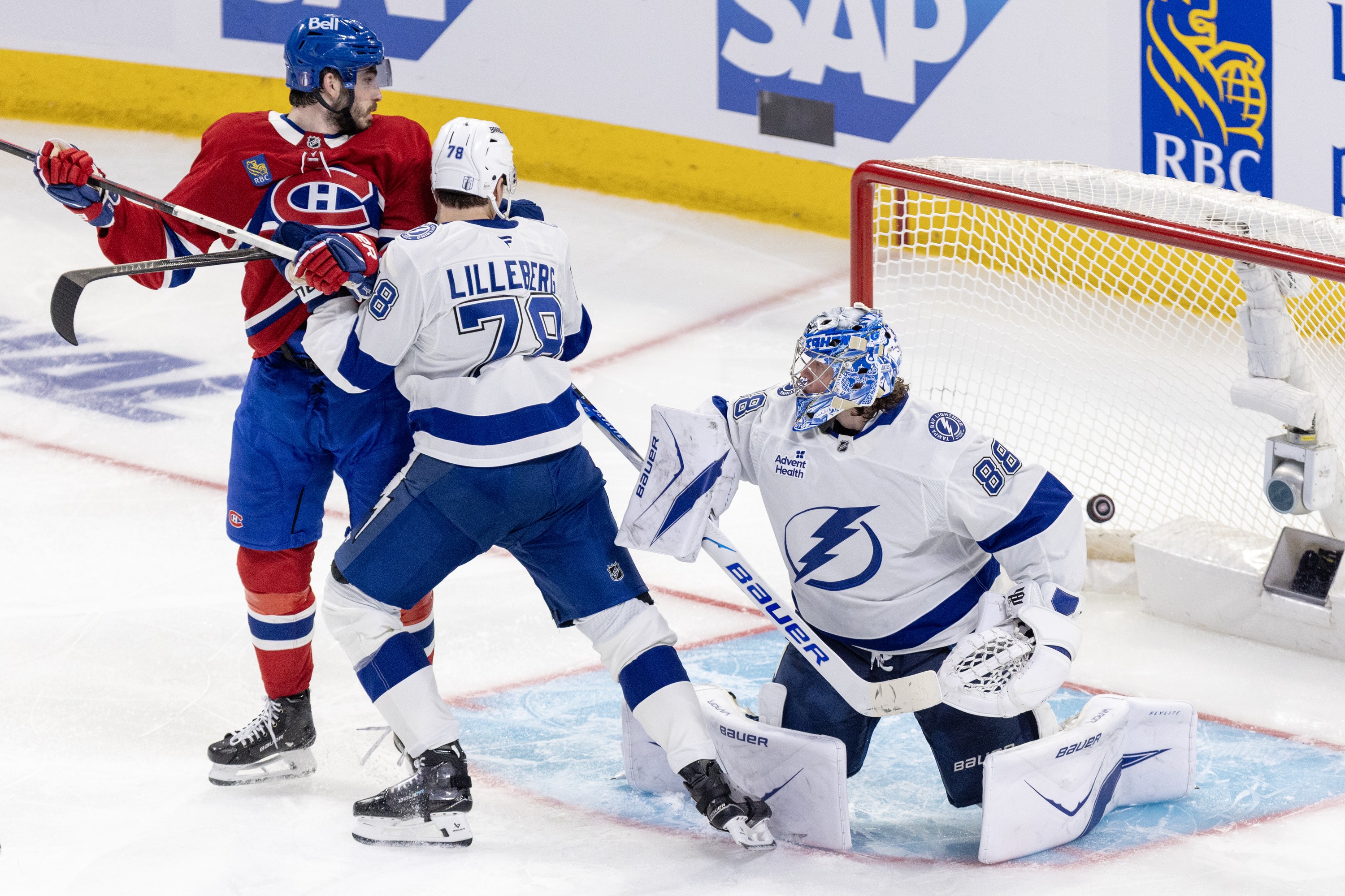 Canadiens' Kirby Dach and Lightning's Emil Lilleberg battle in fron as puck is seen in teh net behind Lightning goalie Andrei Vasilevskiy.