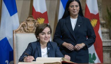 Quebec Premier Christine Fréchette sits while signing a book, with Montreal Mayor Soraya Martinez Ferrada standing behind her.