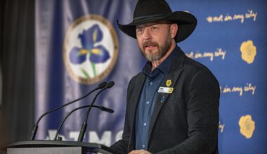 Paul Brandt, wearing a black cowboy hat, stands at a podium with microphones.