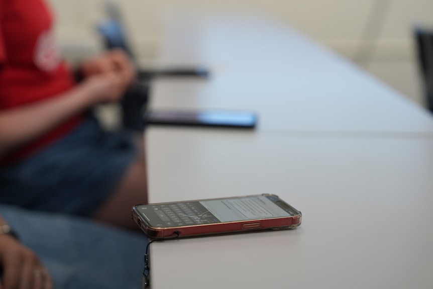 Three mobile phones lined up on a table with unidentifiable owners.