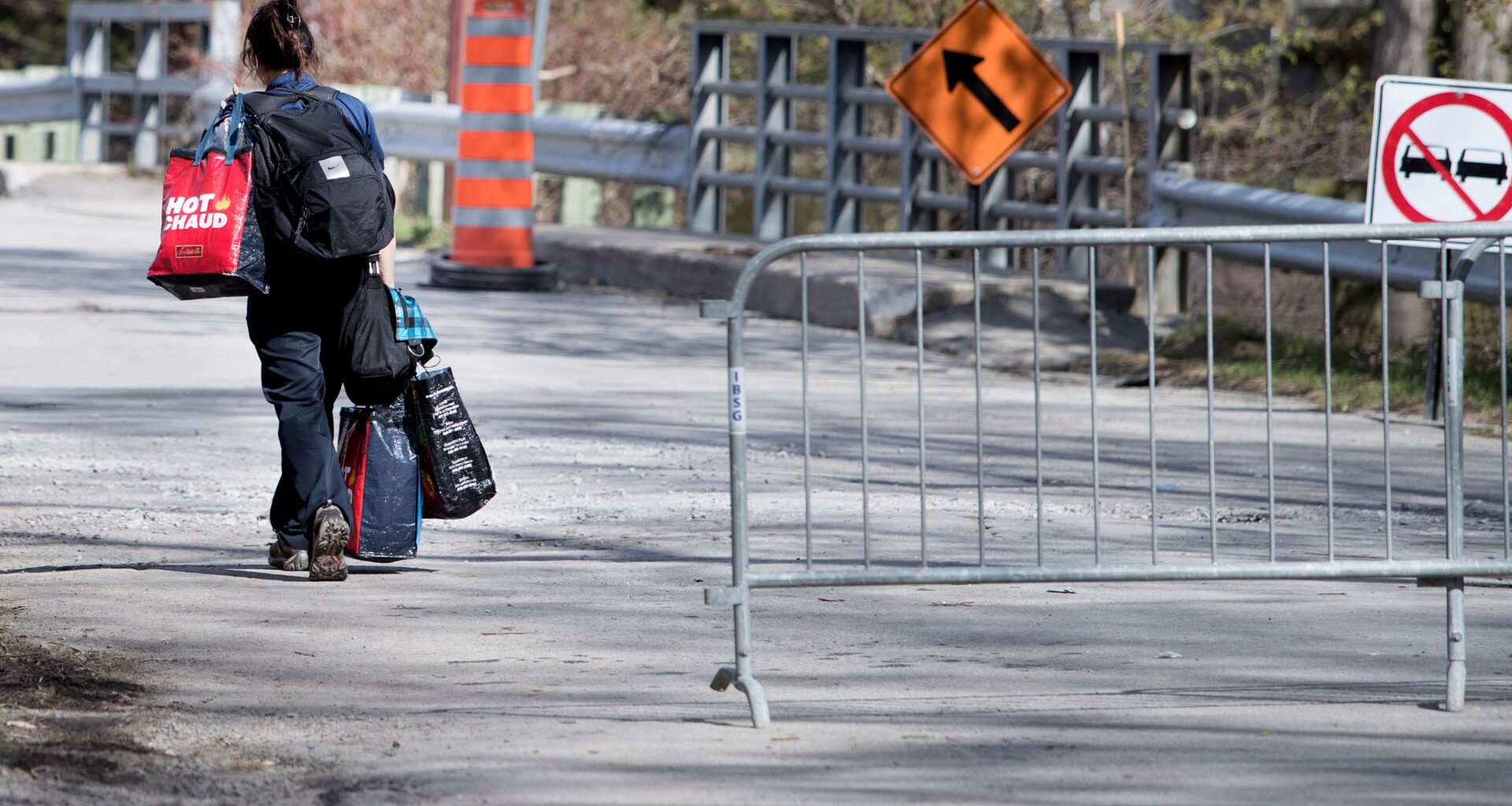 A woman carries bags across a two-lane bridge that is closed to traffic.