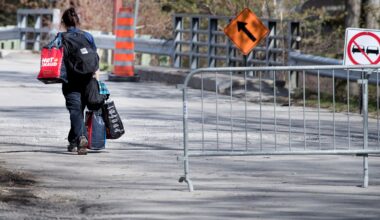 A woman carries bags across a two-lane bridge that is closed to traffic.