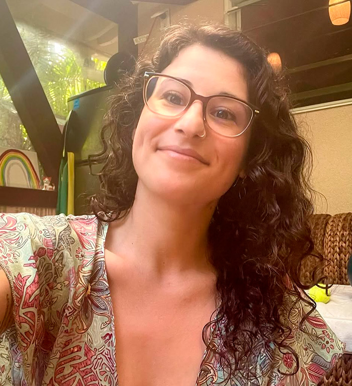 Woman with curly hair and glasses smiling indoors, related to OpenAI CEO Sam Altman lawsuit allegations.