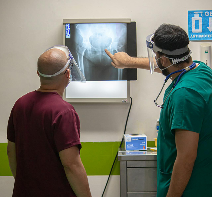 Two healthcare workers wearing face shields examine a hip x-ray in a hospital setting, highlighting hidden hospital truths.