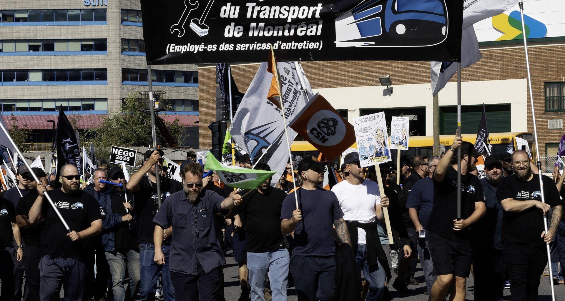 Workers hold up a large banner with the STM maintenance union logo on it.