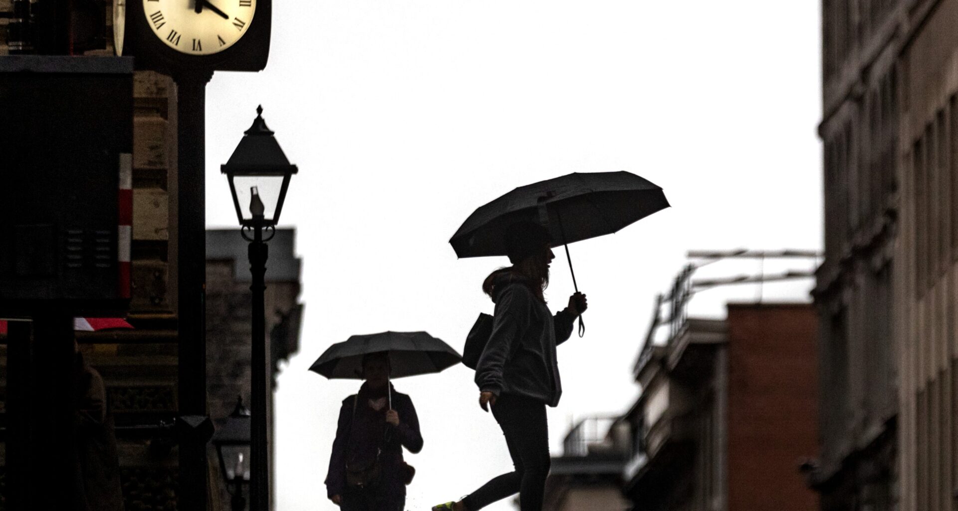 People walk along the street carrying umbrellas with a clock tower in the background.