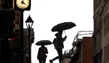 People walk along the street carrying umbrellas with a clock tower in the background.