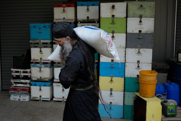 Father Seraphim carries a sack of feed for sheep at the Monastery of St. Augustine and Seraphim of Sarov in the village of Trikorfo, about 236 kilometers (147 miles) northwest of Athens, Friday, March 20, 2026. (AP Photo/Thanassis Stavrakis)
