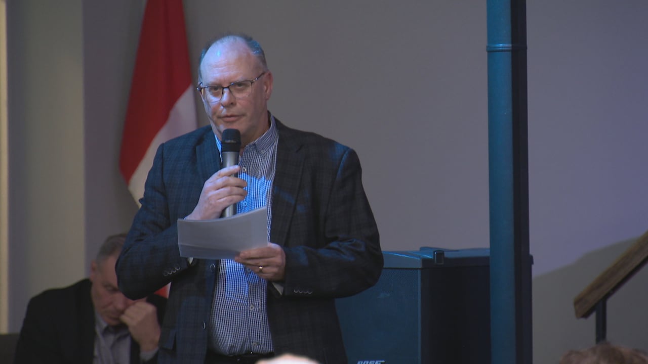 A man speaks into a microphone while holding papers