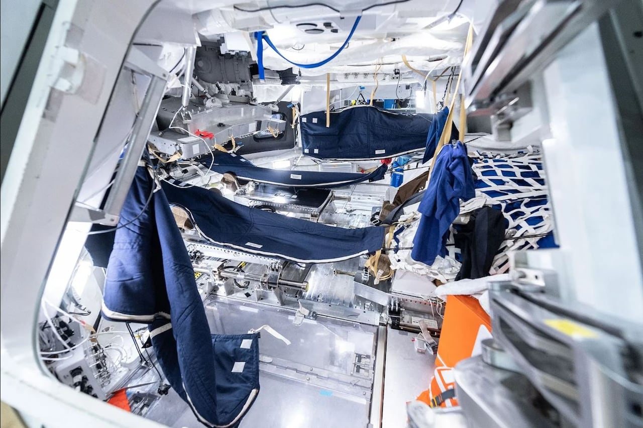 The inside of a space capsule four blue hammock-like sleeping bags hanging from the white walls.