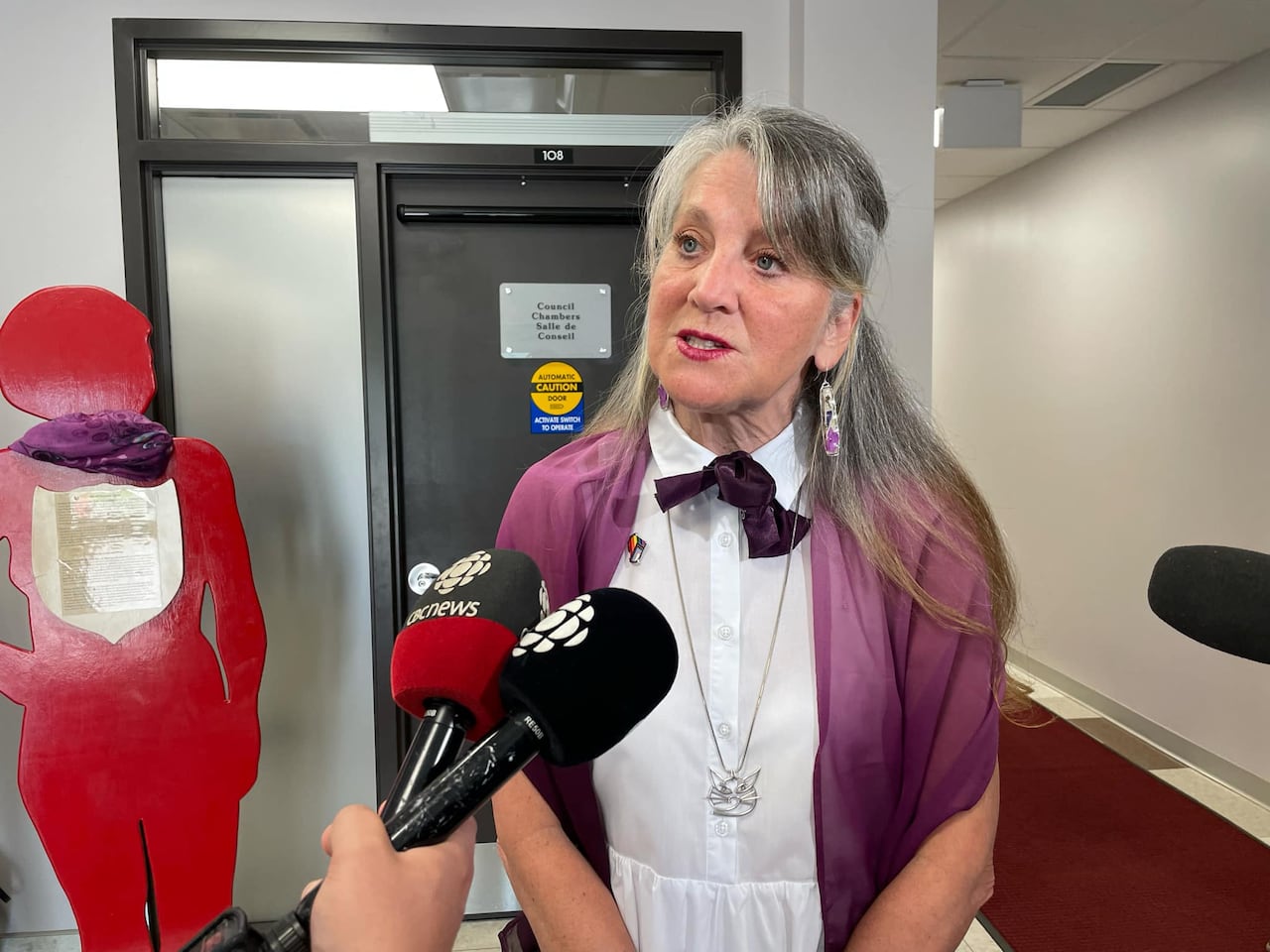 A woman with long grey hair wearing a white dress speaks to reporters.
