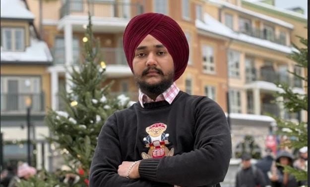 a man in a black sweater with a dark red turban stands on a wintry street
