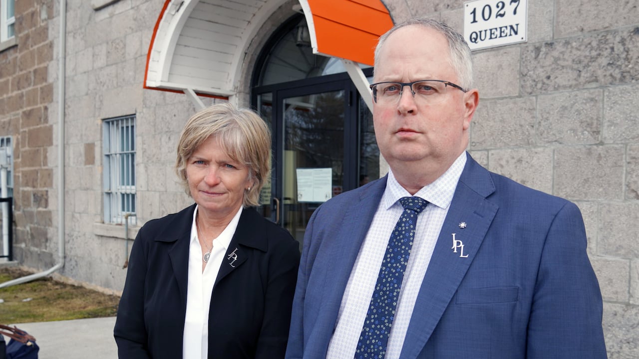 A man and a woman in suits stand outside a stone building.