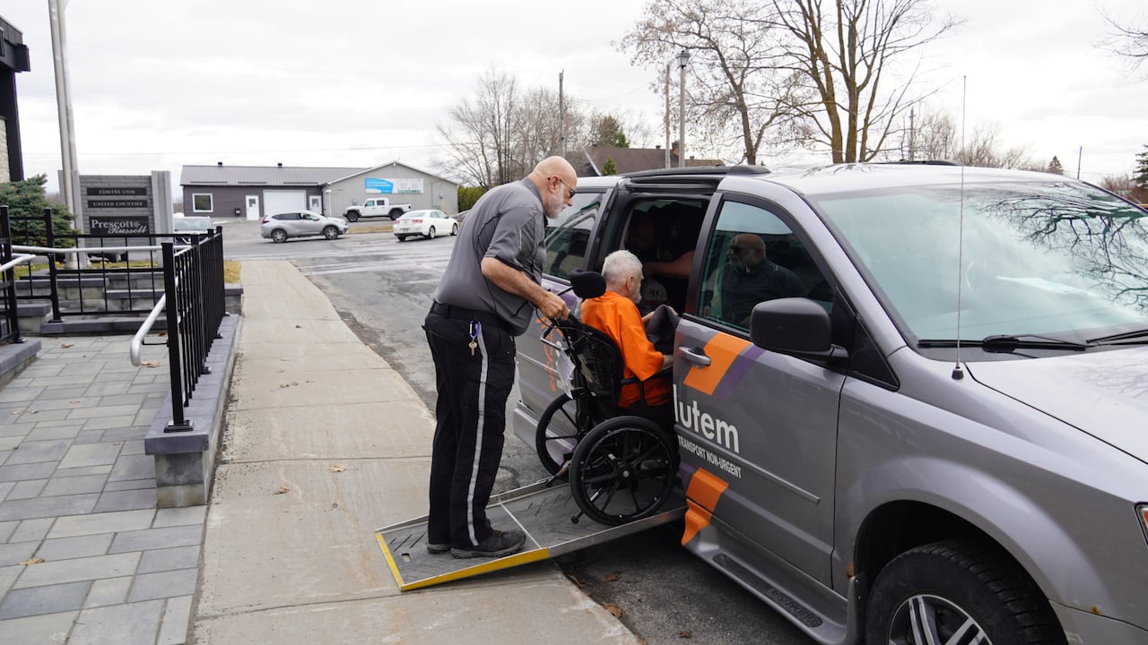 A man pushes another man in a wheelchair into a grey van.