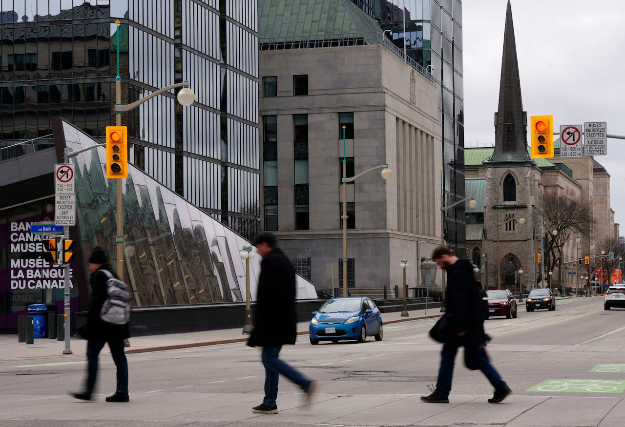 People cross a downtown city street in a cloudy spring day.