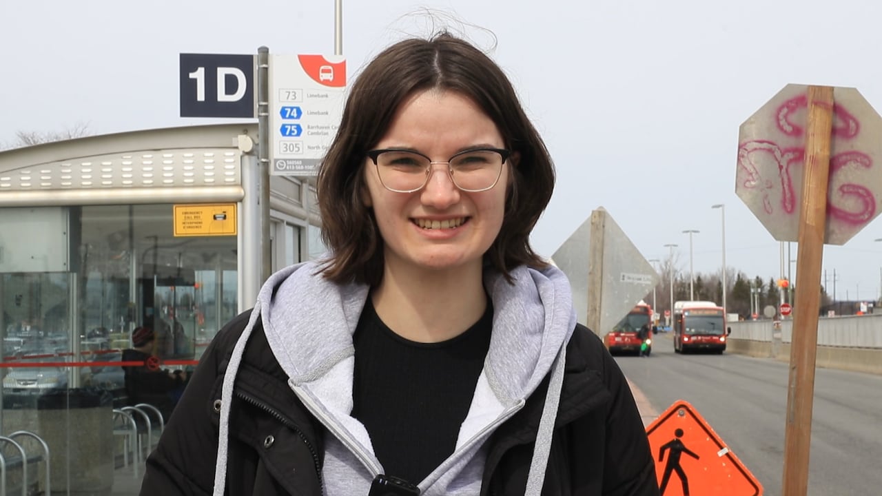 A girl in a black jacket and gray hoodie is pictured in front of an OC Transpo bus stop. 