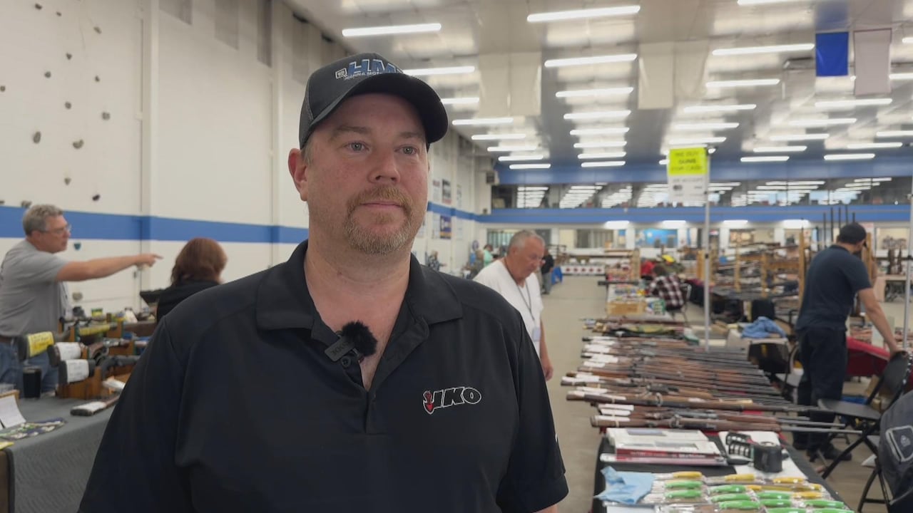 A man wearing a black shirt and a baseball cap looks at the camera.