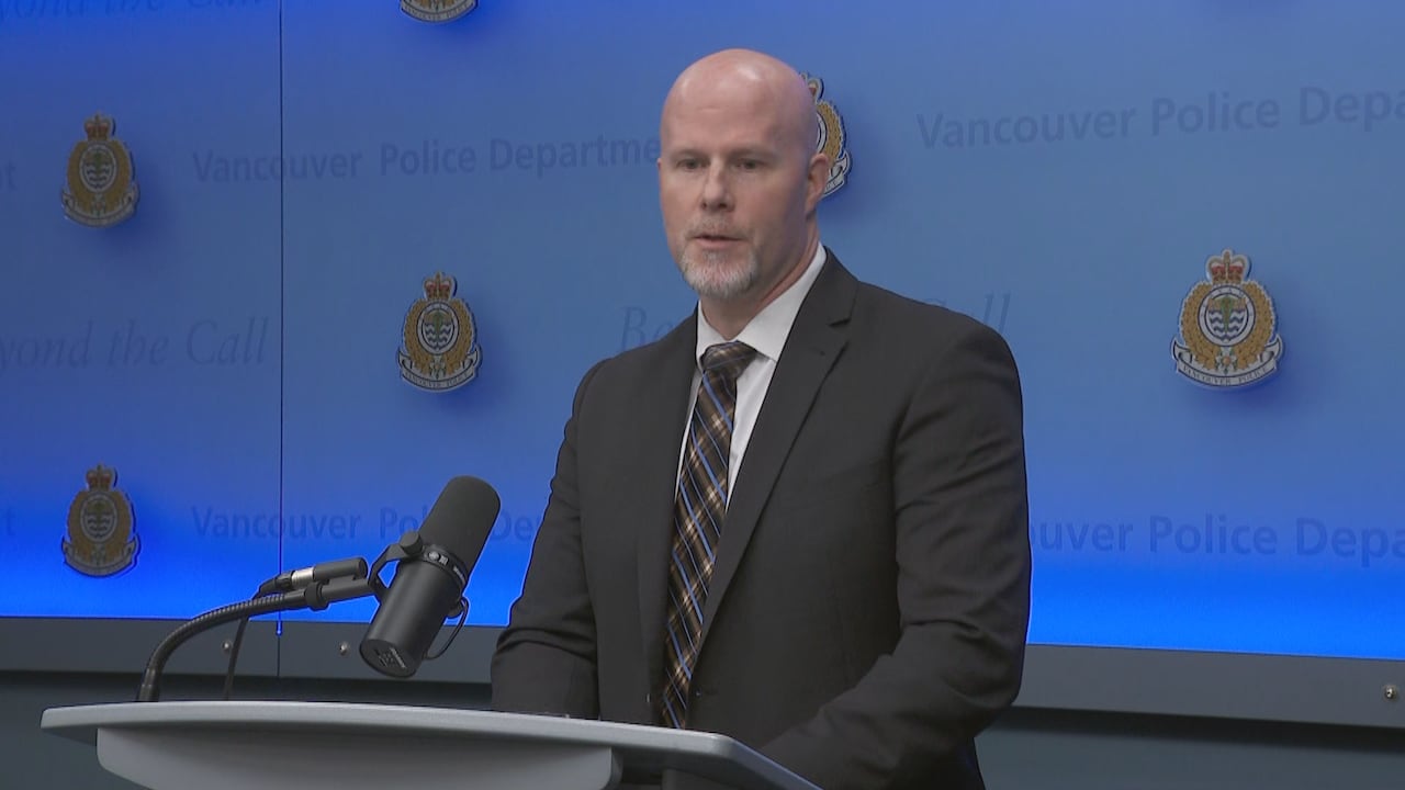 A bald man in a suit speaks at a podium with the Vancouver Police Department logo behind him.