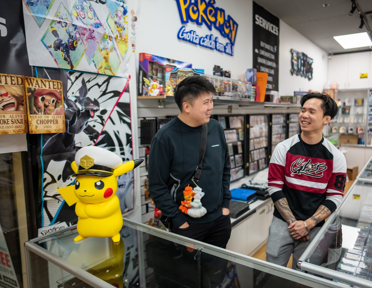 Two men smile at the counter of a trading card store.