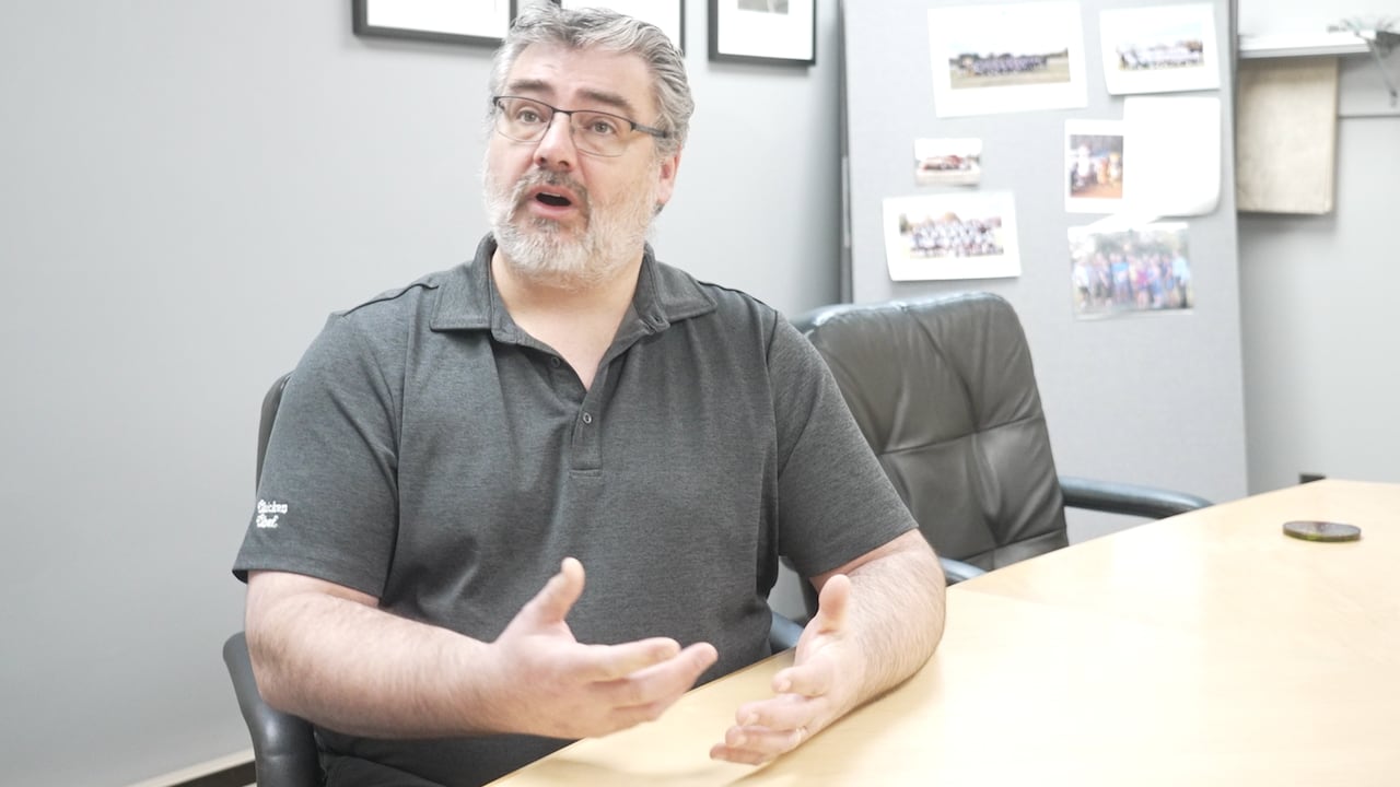 A man sits at a desk and speaks.