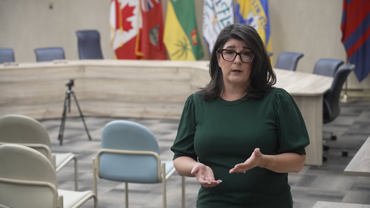 A woman stands in a room and speaks.