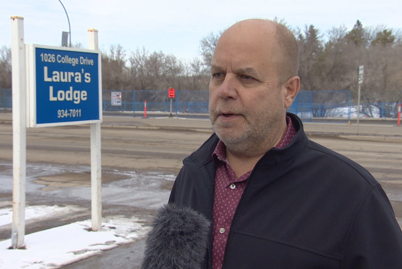 A man stands in front of a sign that says Laura's Lodge.