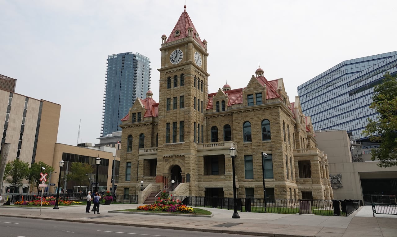 a historic building. two people stand in front looking up at it. there are colourful flowers planted around it 