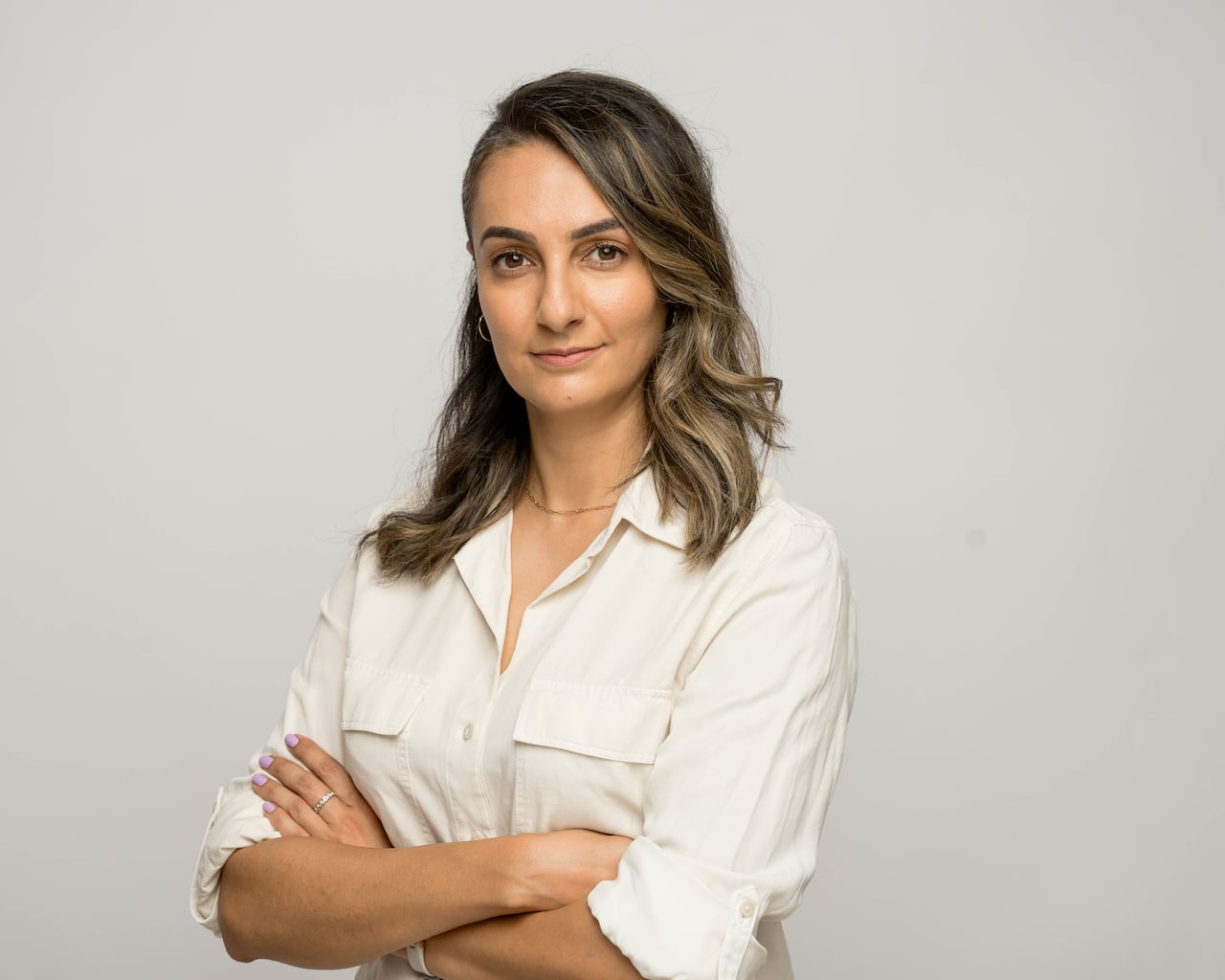 A woman stands in a headshot photo, wearing a white blouse with her hands crossed. 