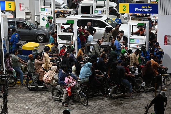 People on motorbikes line up at a gas station at night.