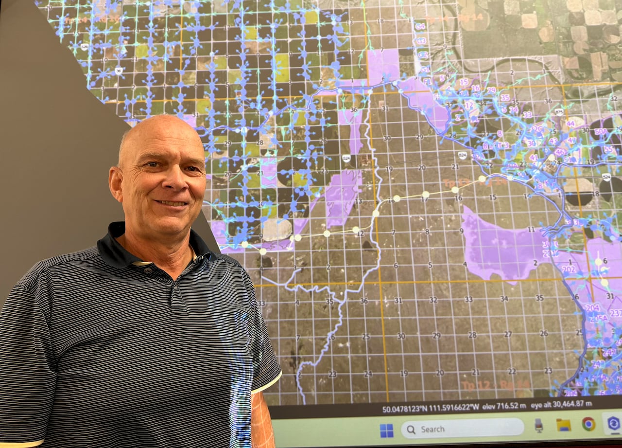 A bald man in a golf shirt smiles in front of a projection of a map with purple patches and blue lines, representing irrigation works.