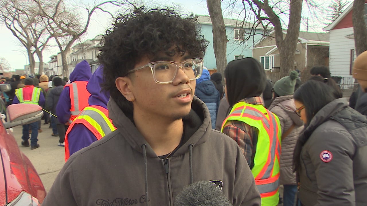 A teenager in a hoodie and glasses speaks into a microphone.