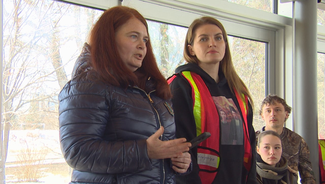 Two women stand side-by-side, as one speaks to a crowd that's out of the camera's view.