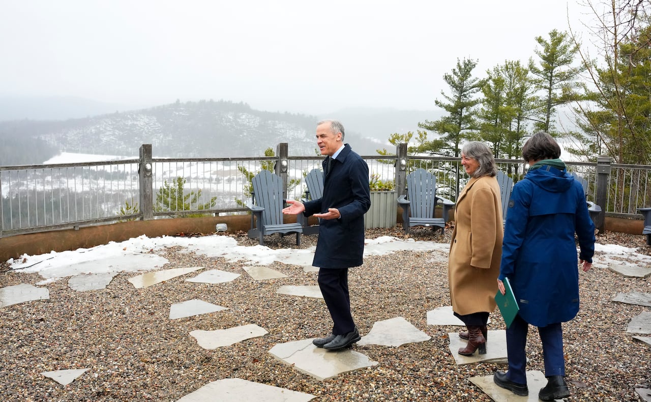 Prime Minister Mark Carney jokes about following the path of stones as he and Environment and Climate Change Minister Julie Dabrusin, middle, and Nathalie Provost, Secretary of State (Nature), arrive to take part in an announcement in Wakefield, Que.