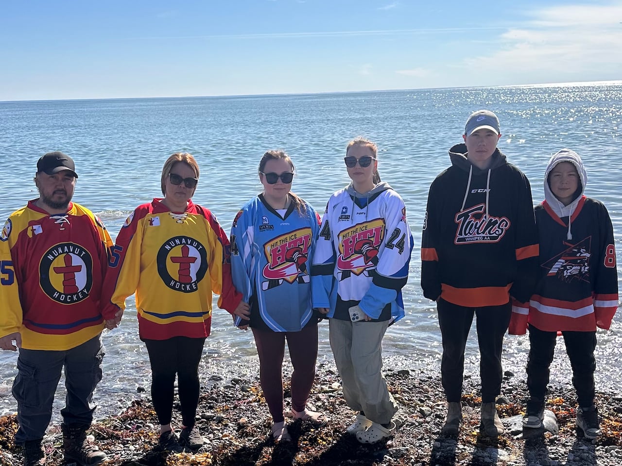 Six people wearing different hockey jerseys stand on the shore of Hudson Bay