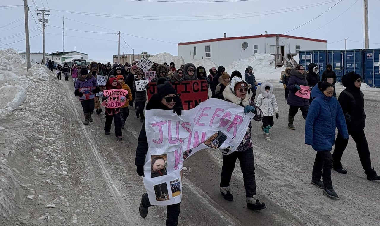 A group of people in winter clothing holding signs that say Justice for Kadin walk down a snowy road.