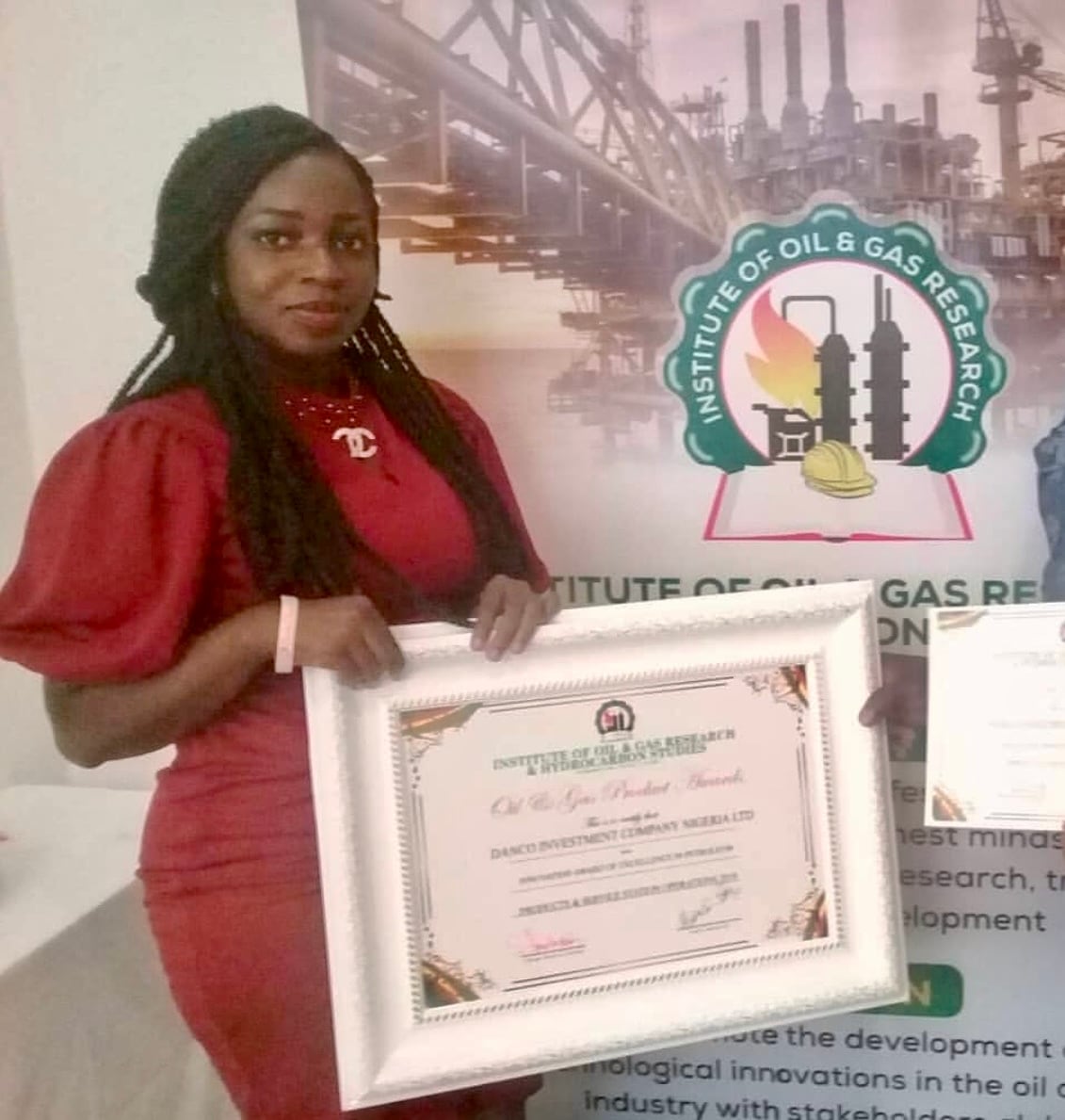 A smiling woman wearing a red dress holds a framed certificate. 