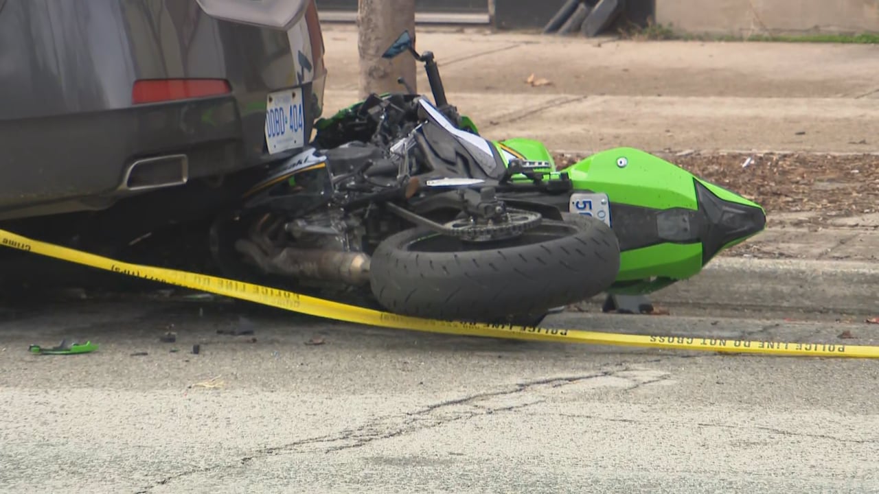 Crushed-up motorcycle on its side on roadway, partially under parked car