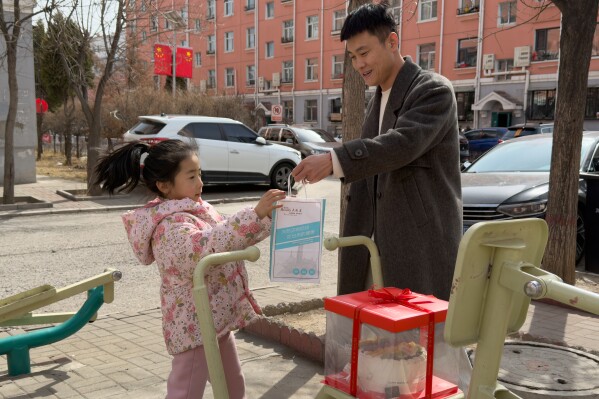 Zhou Hongfei, a coal miner, holds a bag out to his daughter at a residential complex for former and current coal miners in Datong, China, Saturday, March 14, 2026. (AP Photo/Ng Han Guan)