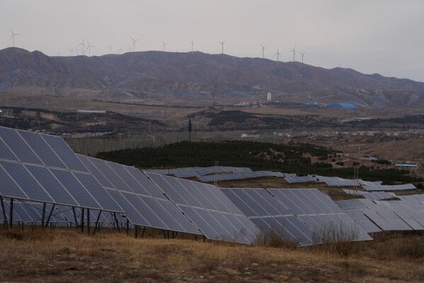 A solar farm operates with wind turbines in the background in Datong, China, Friday, March 13, 2026. (AP Photo/Ng Han Guan)