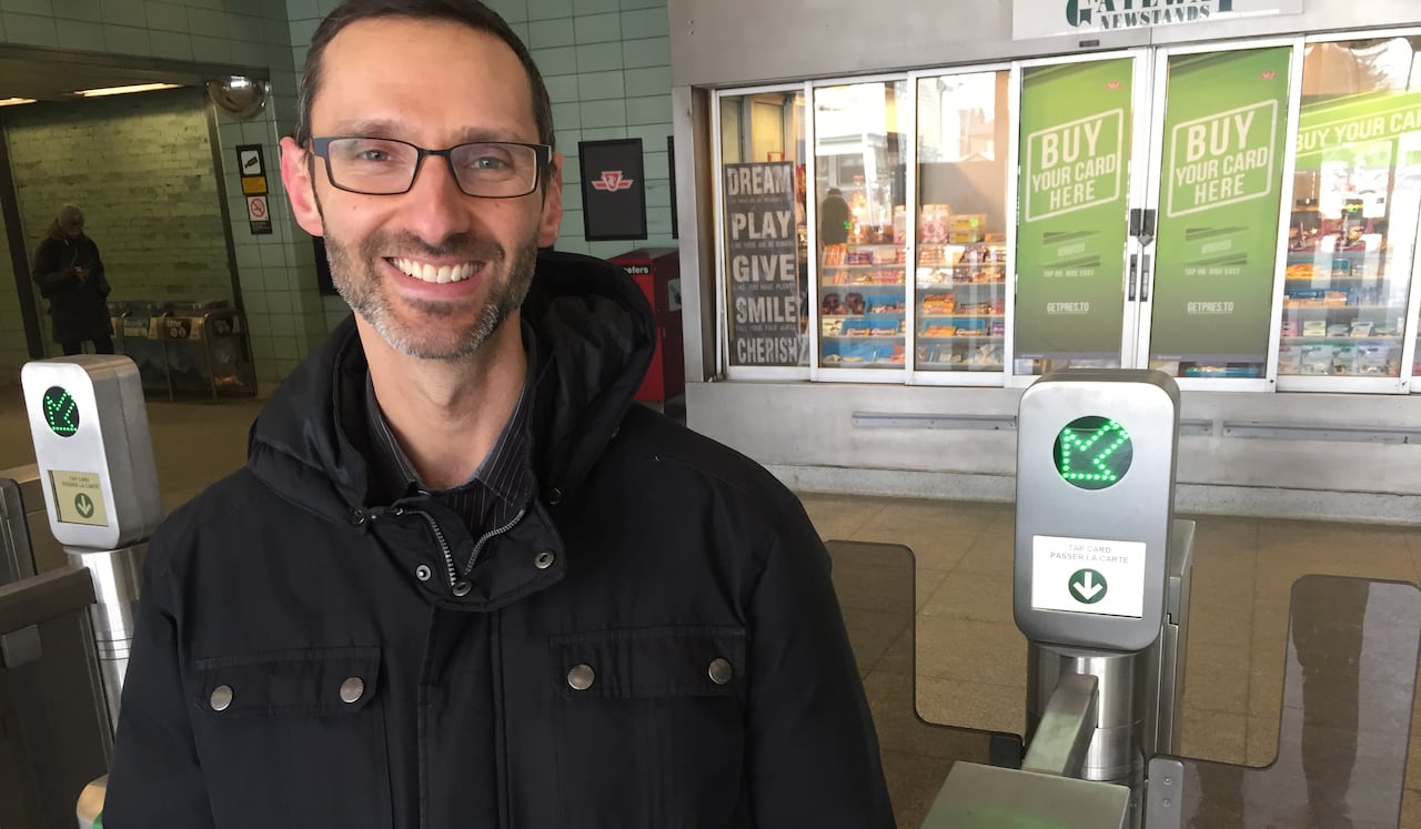 A man stands near a transit turnstile.