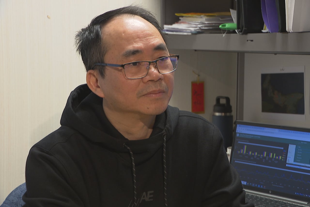 A man sits at a desk in an office with water charts on a computer screen behind him.