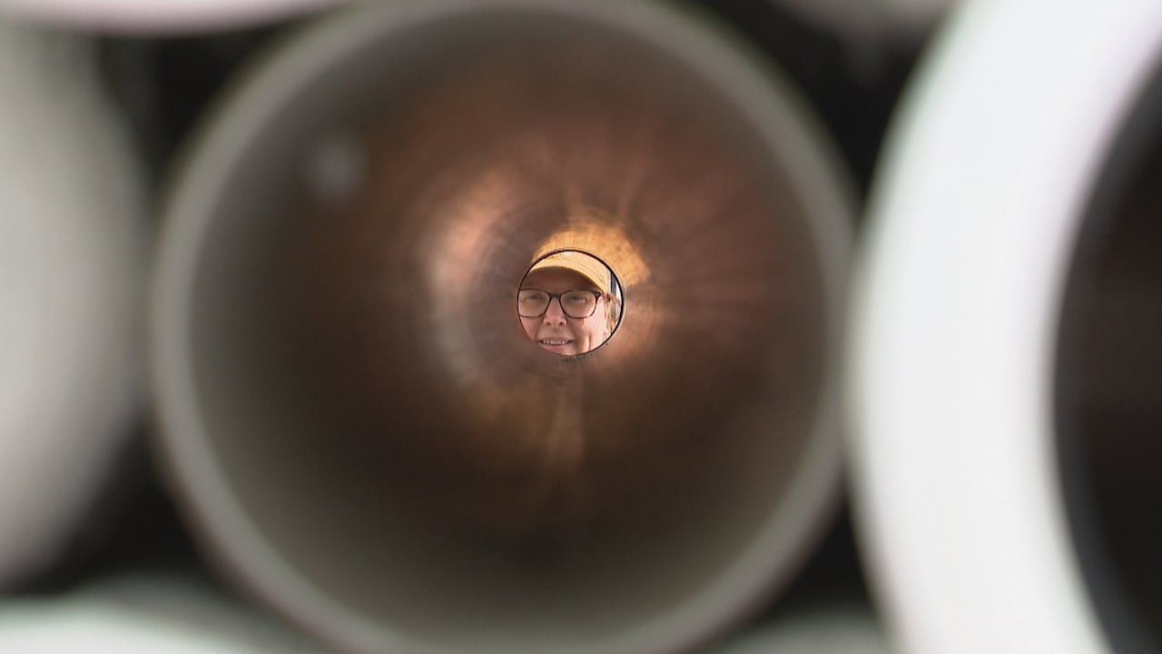 A woman's face is framed in the circular end of a hollow pipe, filmed from the other end of the tube.