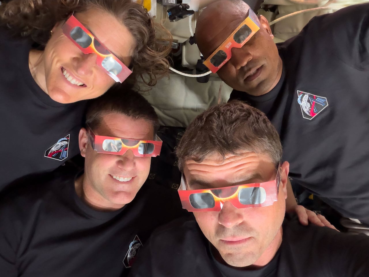 Four astronauts, all wearing eclipse-viewing glasses, smile for the camera