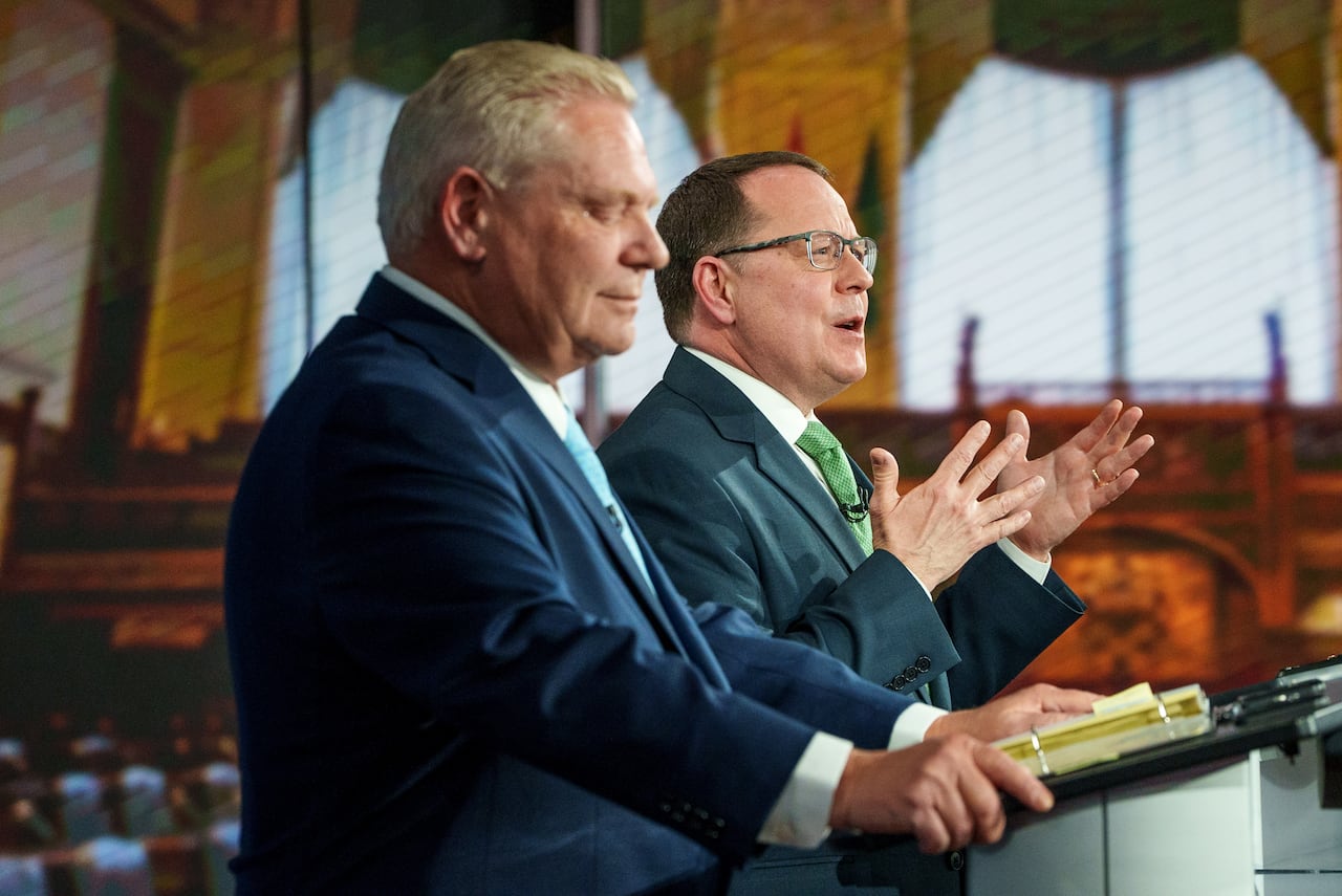 Two men speak at lecterns during a debate.