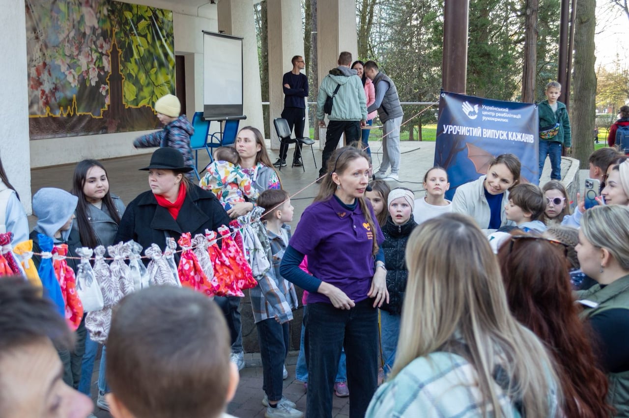 A woman in a purple shirt  stands outside speaking to a group of onlookers, including many children