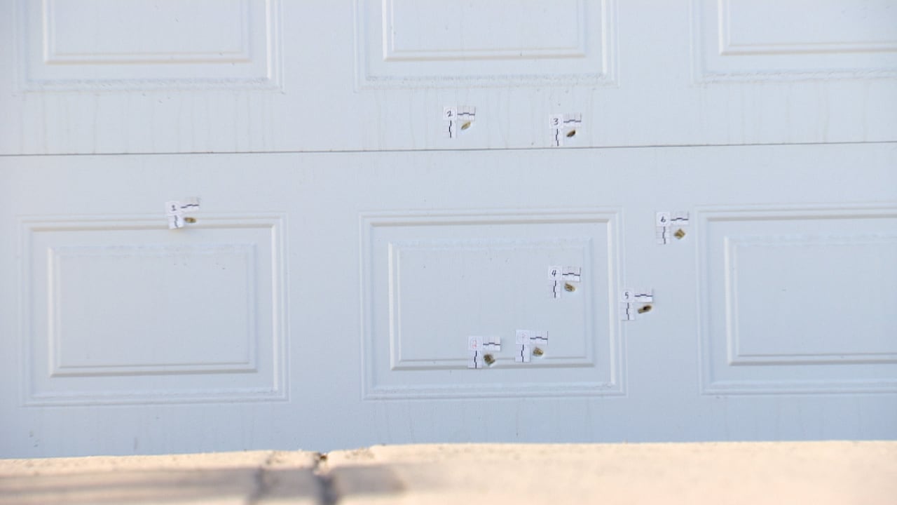 A number of bullet holes in a white garage door