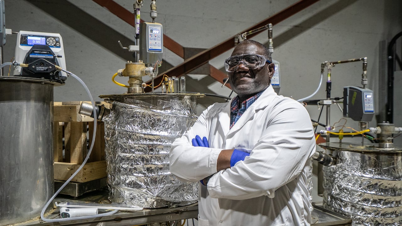 Man in lab coat stands in front of large reactors. 