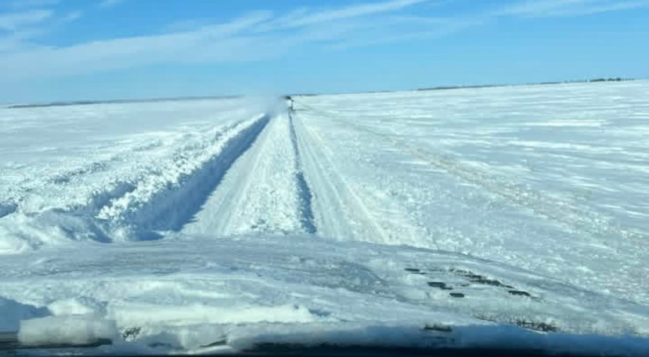 A highway covered in deep snow, seen through a vehicle's windshield.