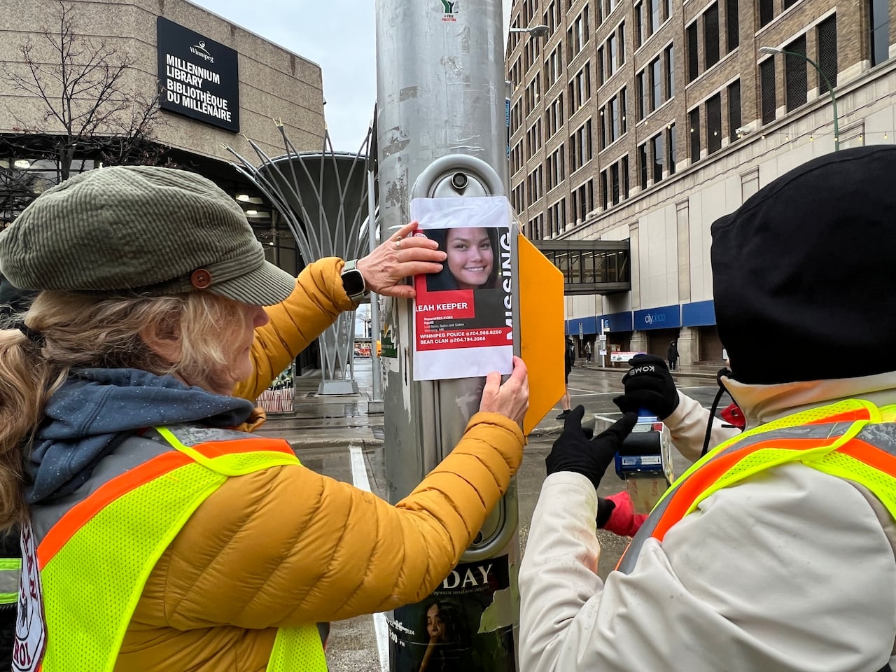 Two people paste a poster on a traffic light in Winnipeg's downtown